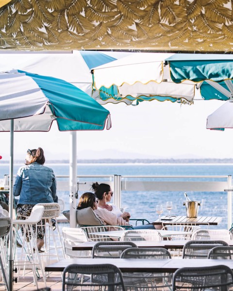 People relax at Shoal Bay Country Club under striped umbrellas. The scene conveys a calm, leisurely vibe.
