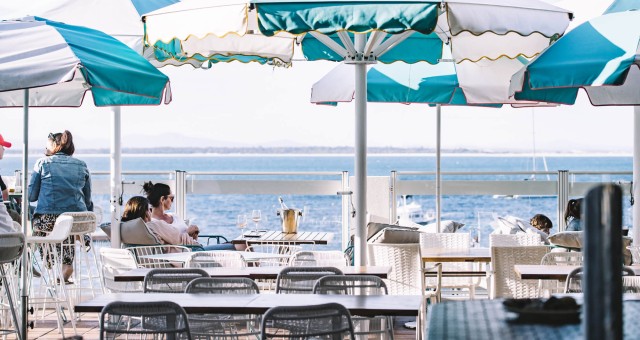 People relax at Shoal Bay Country Club under striped umbrellas. The scene conveys a calm, leisurely vibe.