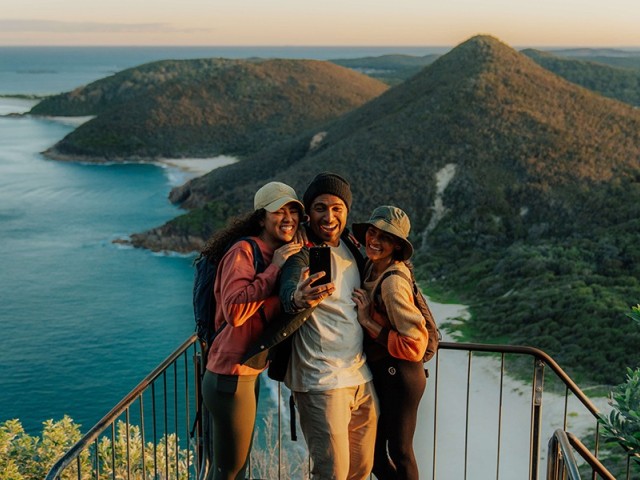 Three people stand overlooking mountains from Tomaree Headland Walk.